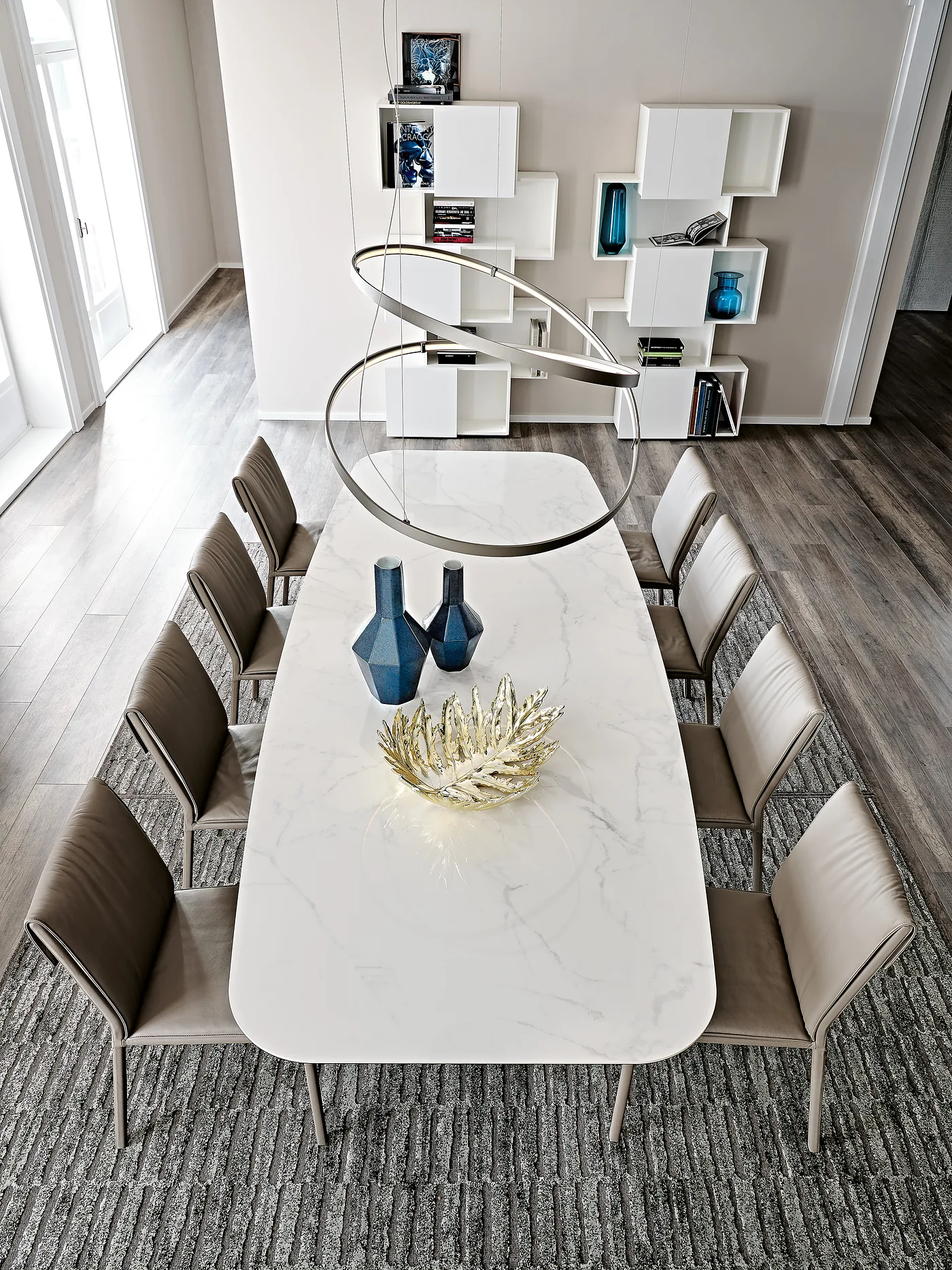 Longue table en céramique claire sur piètement croisé, dix chaises en cuir brun, vue en plongée
