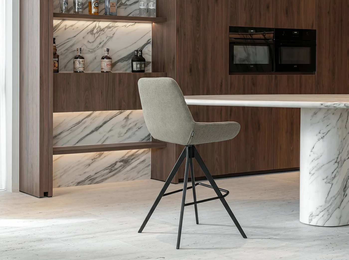 Tabouret de bar enveloppant en tissu gris clair, pieds noirs et repose-pieds, devant un îlot en marbre
