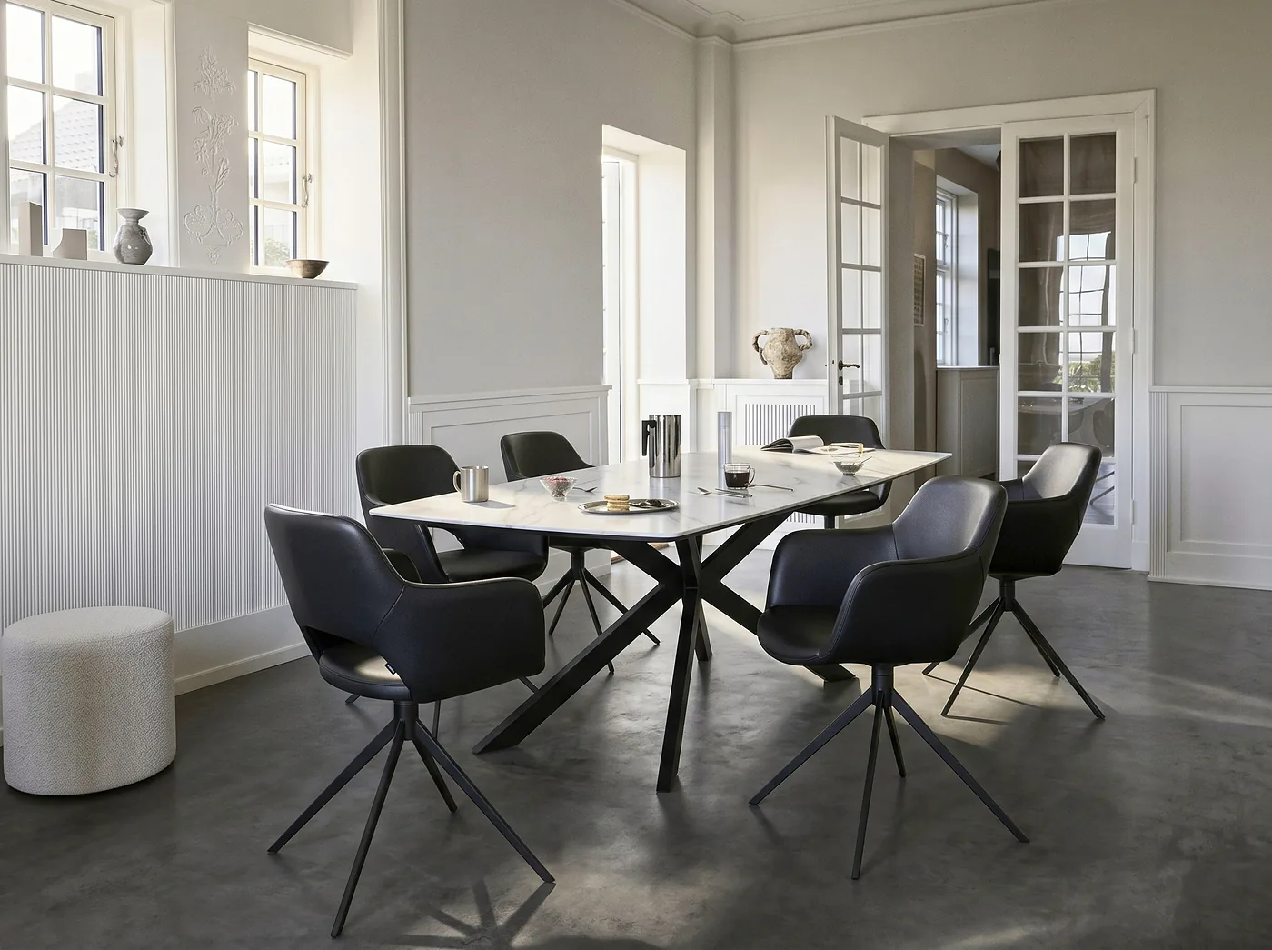 Chaises pivotantes en cuir noir autour d’une table au plateau blanc sur pieds croisés