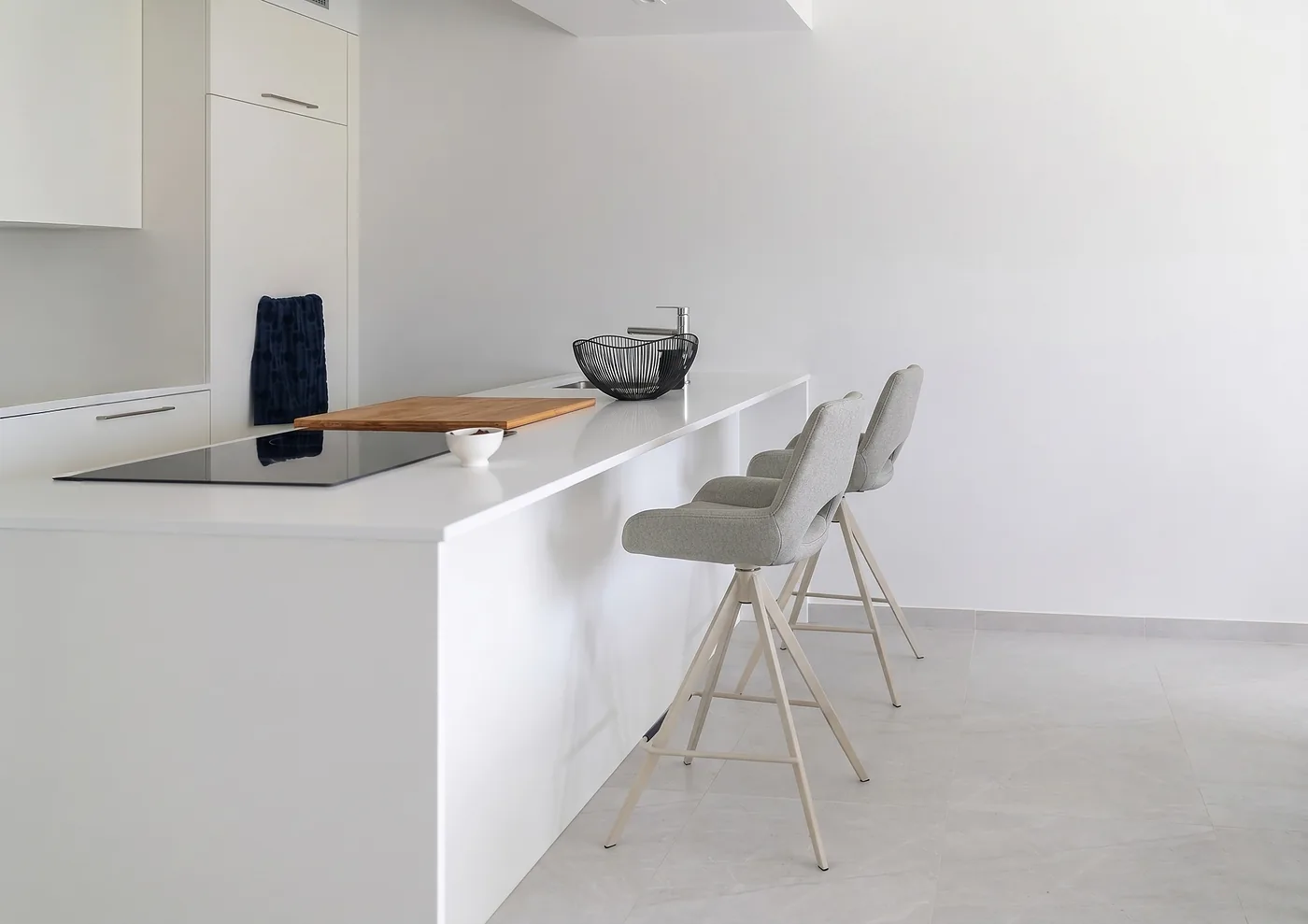 Tabouret de bar en tissu beige capitonné, piétement noir, devant une cuisine sombre