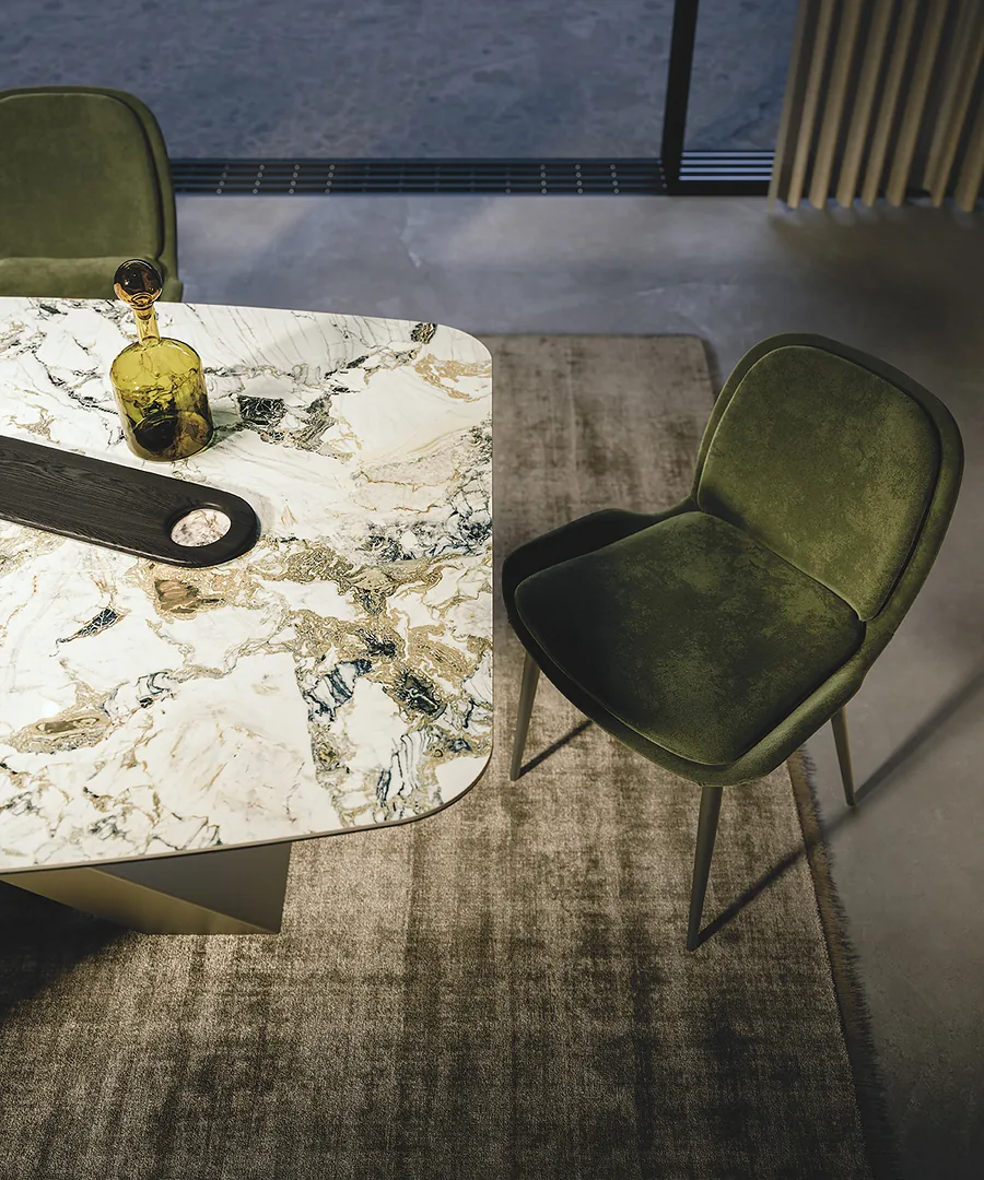 Coin du plateau en céramique marbrée, vu de dessus, avec une chaise en velours vert