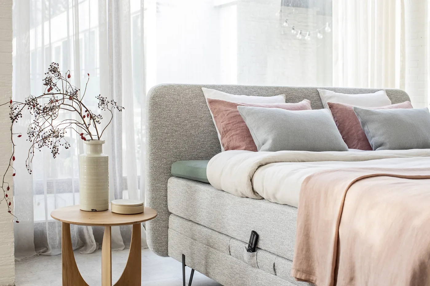 Boxspring en tissu gris chiné, coussins vieux rose et gris bleu, chevet rond en bois clair